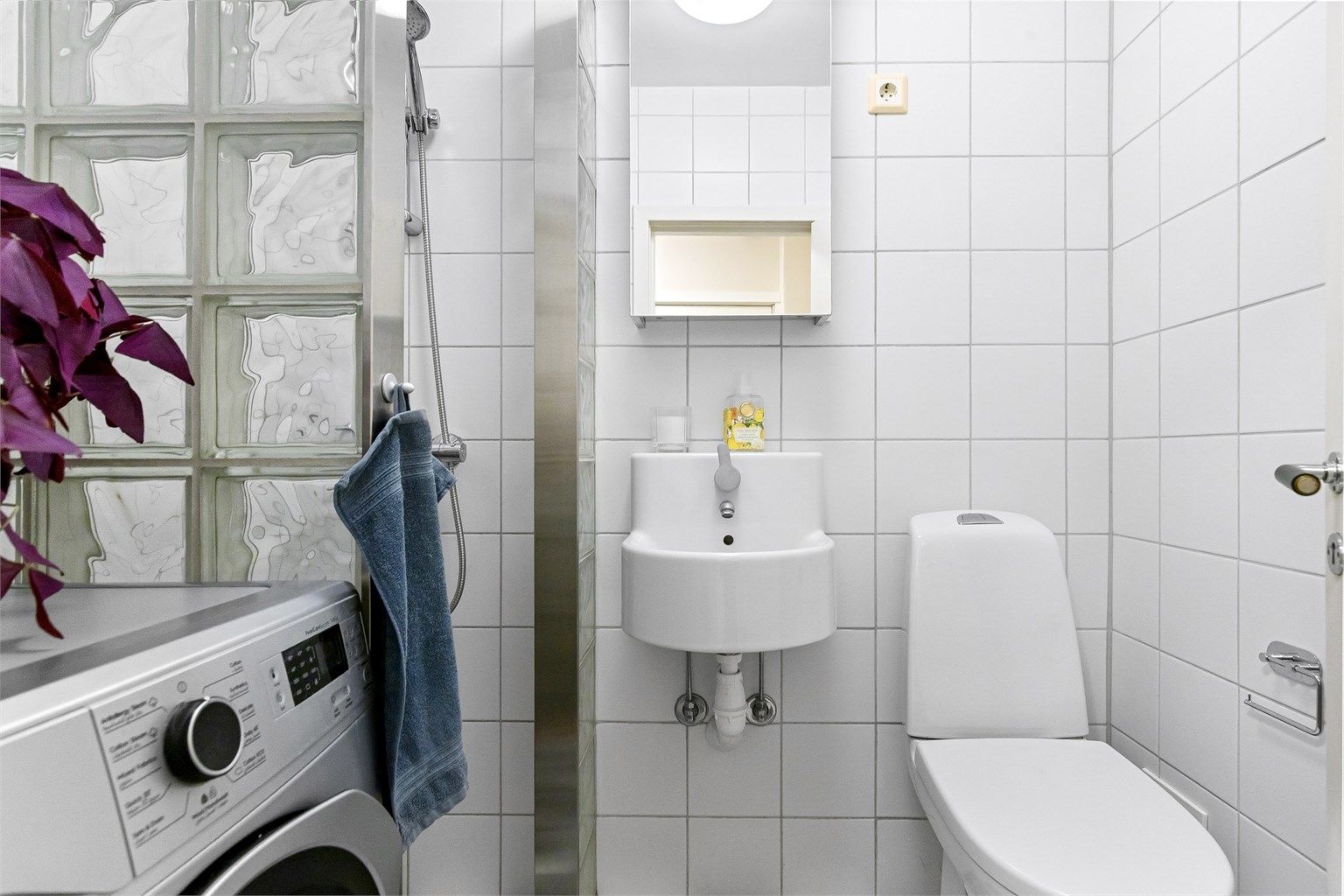 Badet er utstyrt med dusjhjørne av glassbyggerstein, vegghengt servant og speilskap.