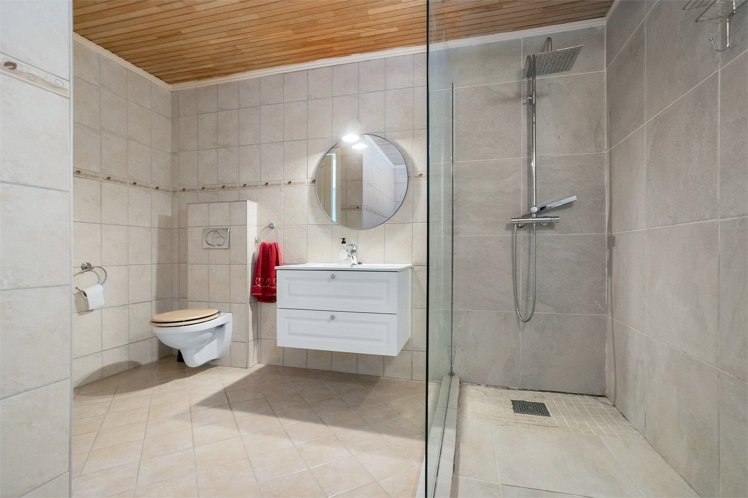 Badet har vegghengt servantskap med skuffer, ovenpåliggende servant med ett-greps armatur, speil og overbelysning på vegg.