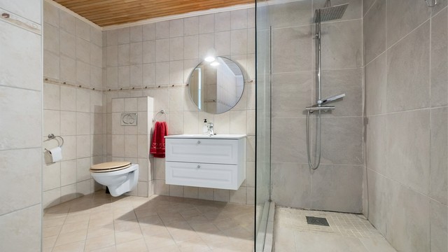 Badet har vegghengt servantskap med skuffer, ovenpåliggende servant med ett-greps armatur, speil og overbelysning på vegg.