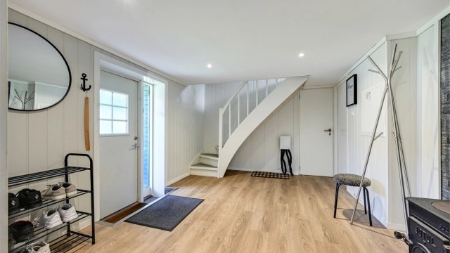 Romslig hall med malt tretrapp opp til hovedetasjen. Ytterdøren ble skiftet i 2017.