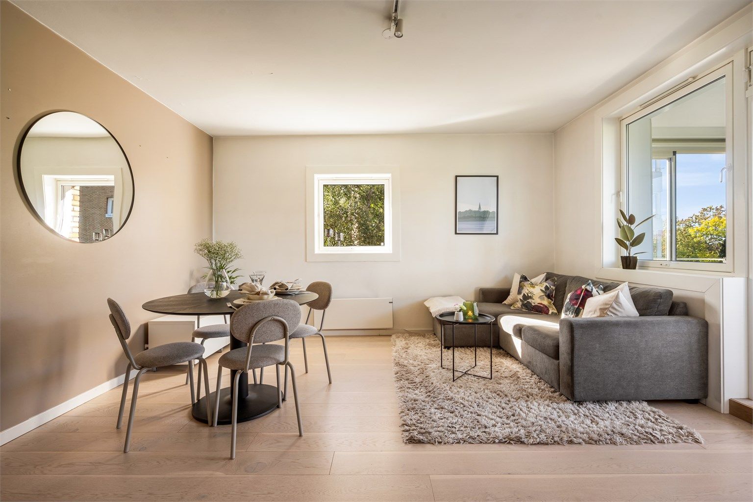 Lys og innbydende stue med lune fargetoner, store vindusflater og en smart planløsning som gir god plass til både sofagruppe og spisebord.