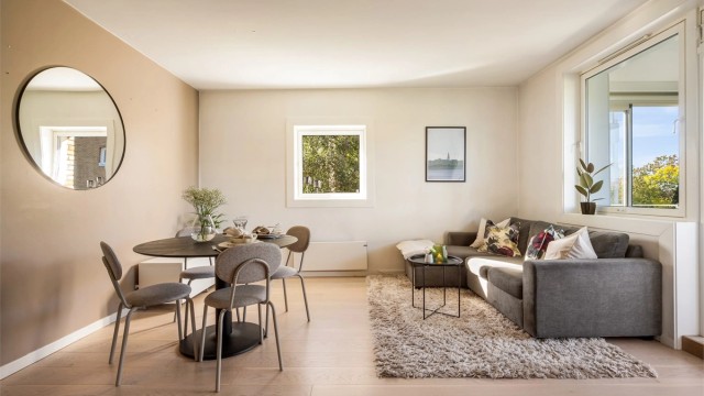 Lys og innbydende stue med lune fargetoner, store vindusflater og en smart planløsning som gir god plass til både sofagruppe og spisebord.