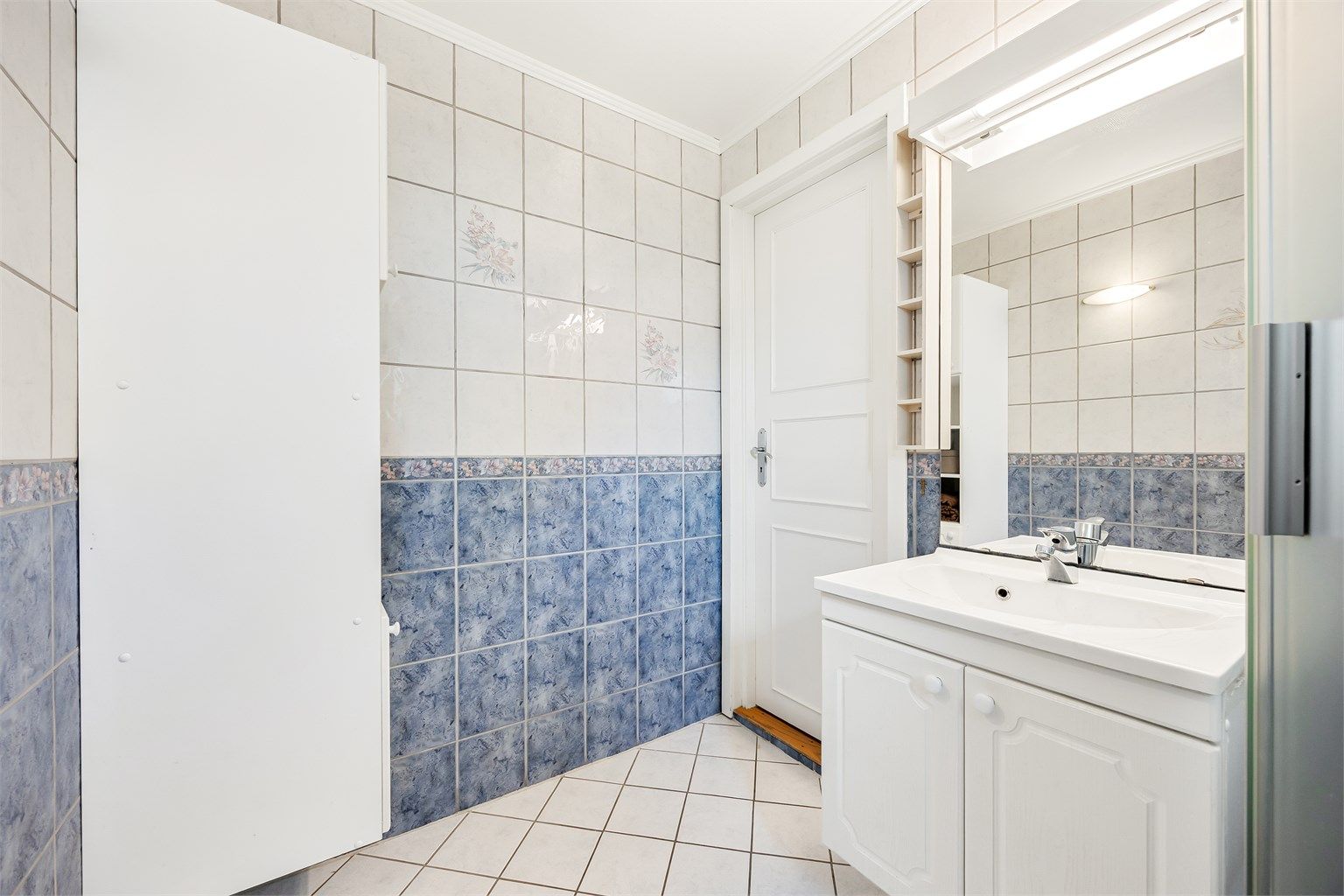 Badet er innredet med servant, speil med belysning og et praktisk høyskap.