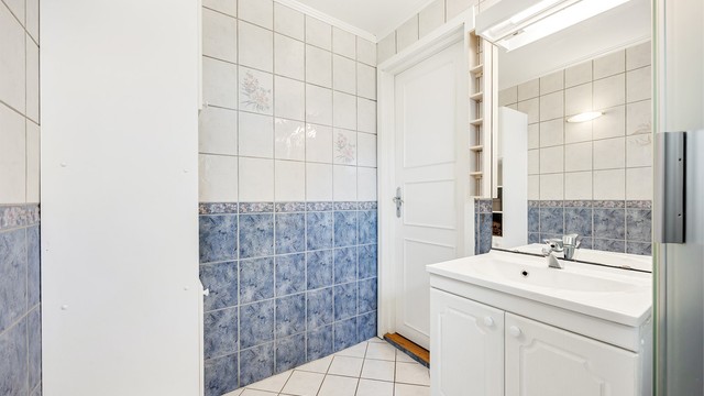 Badet er innredet med servant, speil med belysning og et praktisk høyskap.