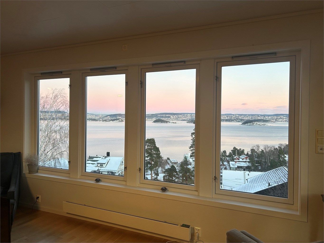 Selgers vinterfoto: Store vinduer i stuen gir flott utsikt mot Oslofjorden, med rosa lys og snødekte omgivelser som skaper en stemningsfull og unik atmosfære.
