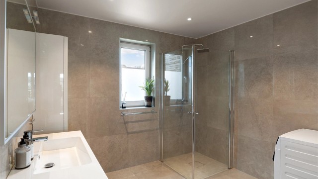 Badet er innredet med dusjhjørne med svingbare glassdører, vegghengt toalett og har opplegg for vaskemaskin.