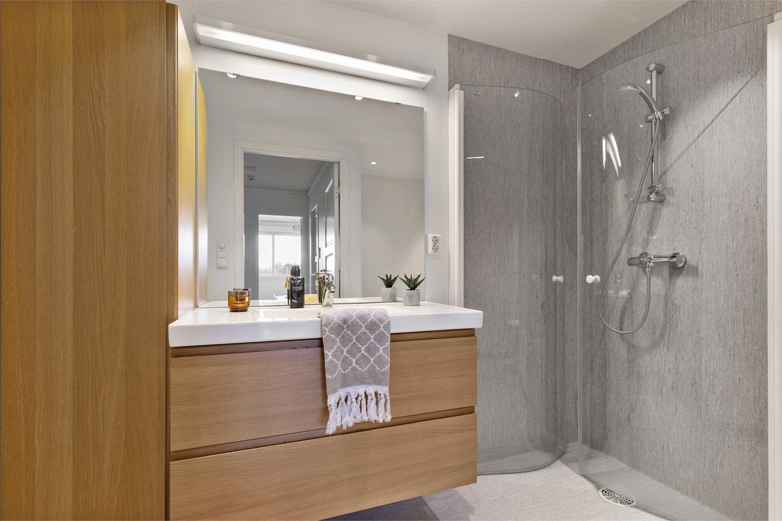 Badet ble oppgradert i 2011 og har en moderne innredning i eikefinish, stor servant og godt med oppbevaringsplass. Speilløsningen med lyslist gir rommet en lys og åpen følelse.