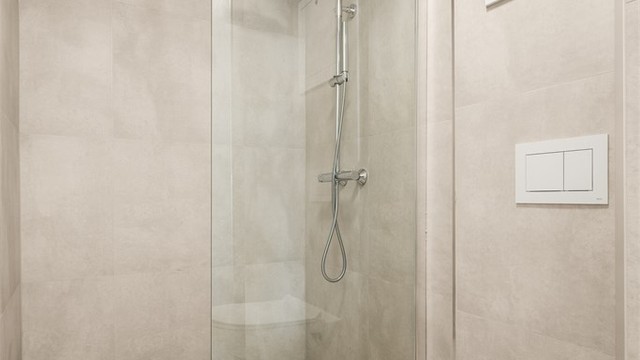 Dusjhjørne med moderne flisvalg. Badet har mekanisk avtrekk.