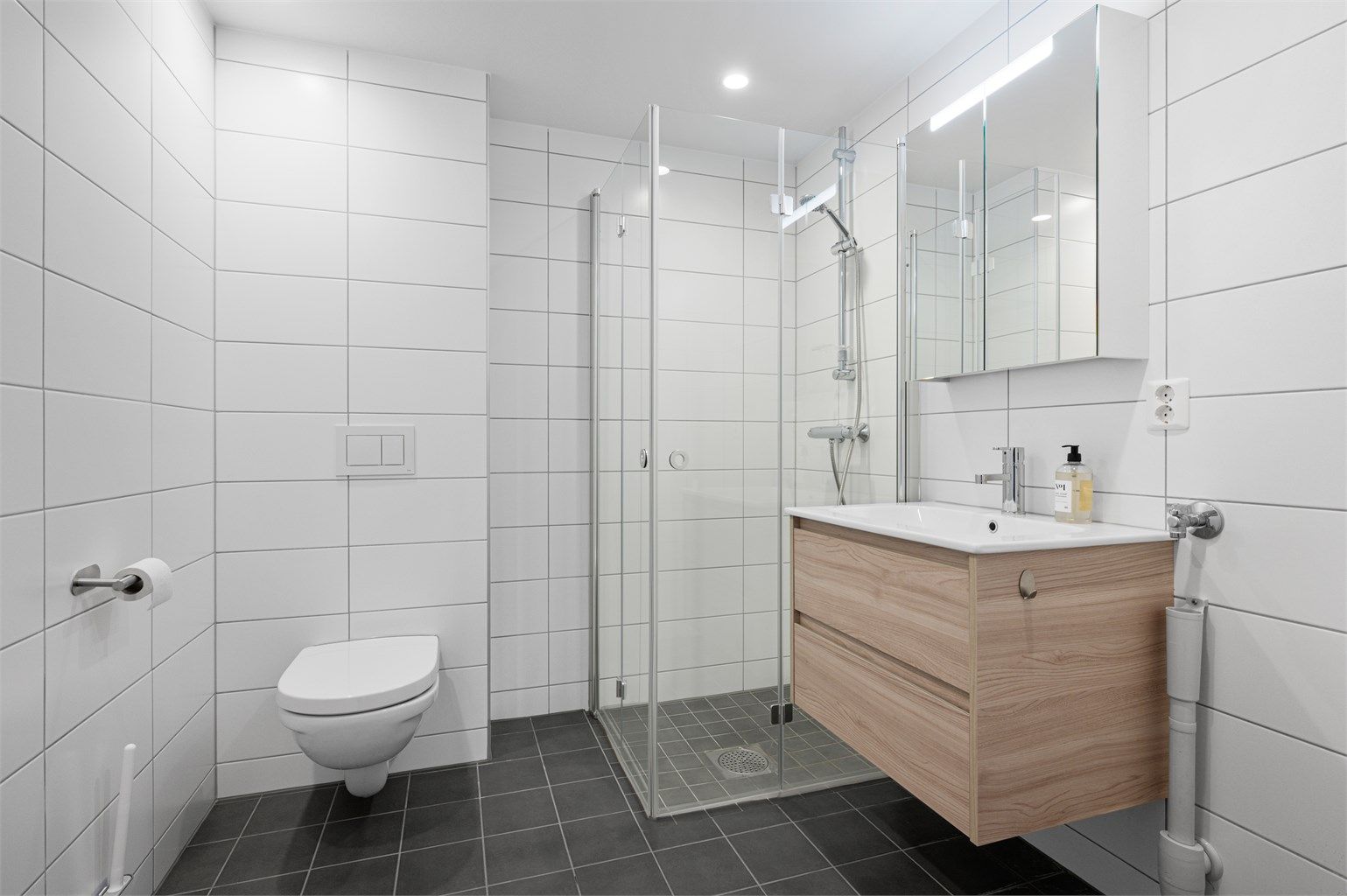 Pent flislagt bad på 4,7 kvm med gulvvarme, downlights og opplegg for vaskemaskin. Videre er badet innredet med servantskap med overskap, dusjhjørne og vegghengt toalett. 