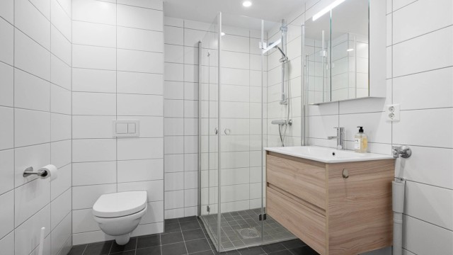 Pent flislagt bad på 4,7 kvm med gulvvarme, downlights og opplegg for vaskemaskin. Videre er badet innredet med servantskap med overskap, dusjhjørne og vegghengt toalett.