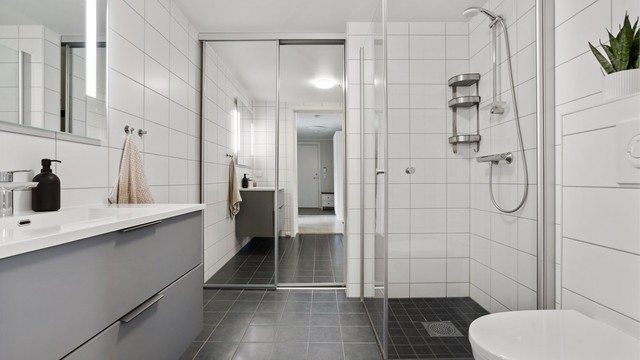 Baderomsinnredning med servantskap, speil med belysning og vegghengt toalett.