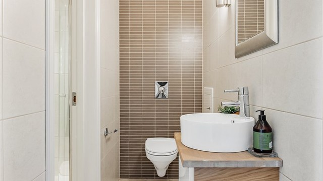 Toalettrom med flislagt gulv med varme. Vegghengt servantinnredning. Vegghengt toalett. Mekanisk avtrekk med ventil i vegg.