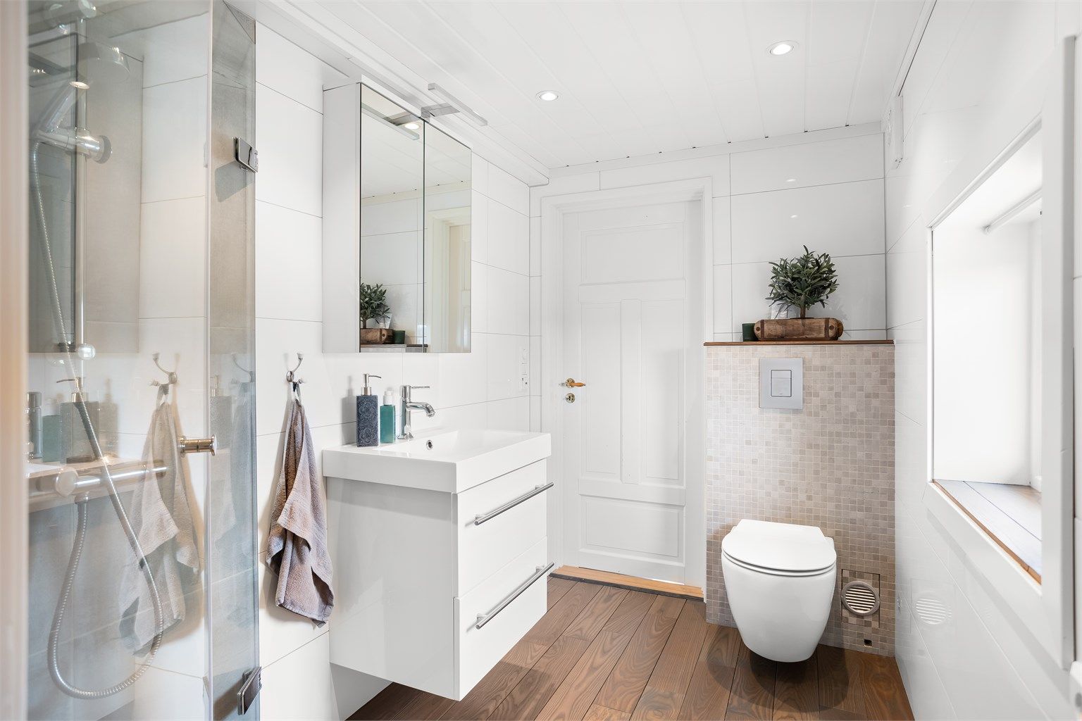 Delikat baderom fra 2016 med flislagte vegger, gulvvarme, vegghengt toalett og opplegg for vaskemaskin/tørketrommel.