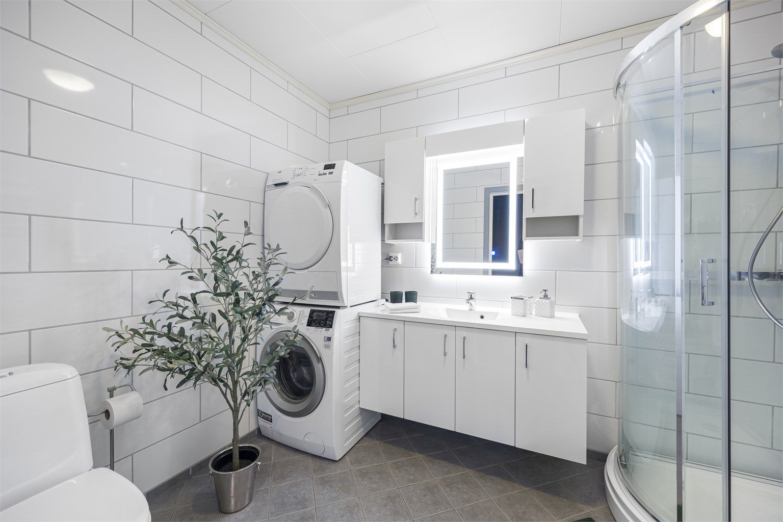 Badet er romslig og utstyrt med servantinnredning, dusjkabinett, toalett og opplegg for vaskemaskin. 