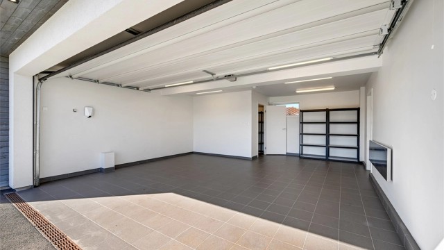 Integrert og isolert garasje med flislagt gulv og elbillader. Varmekabel er lagt i innkjørselen foran porten.