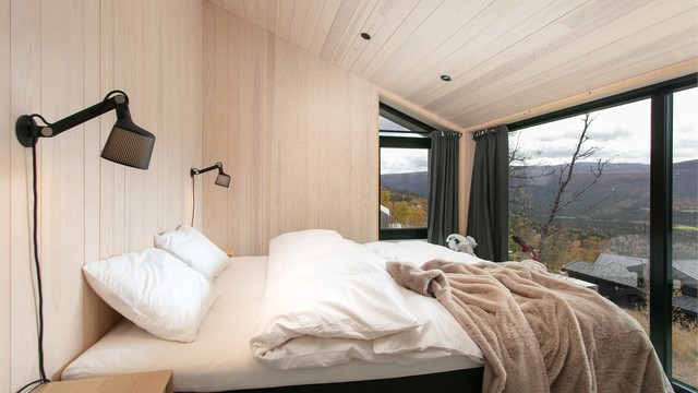 Soverom i loftsetasjen med skråtak og vindusflater mot fjellandskapet.