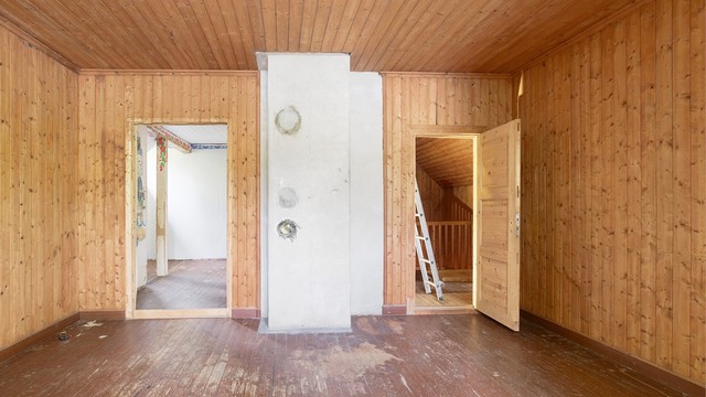 Stort soverom med synlig pipe og gjennomgående treverk på vegger og himling.
