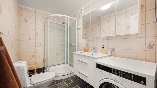 Badet i den minste delen/leilighten er flislagt, har gulvvarme, dusjkabinett og opplegg for vaskemaskin.