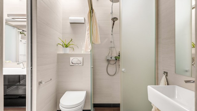 Badet nærmest gangen er innredet med vegghengt toalett og dusjnisje i frostet glass, to-greps dusjarmatur på vegg og regnfallsdusj