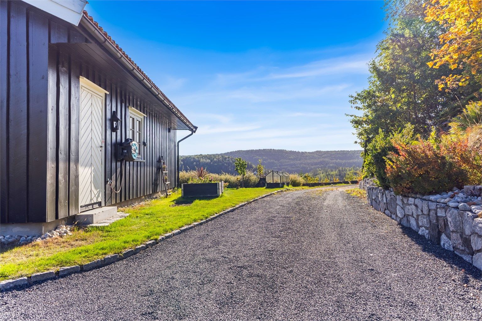 Gruset innkjørsel rammet inn av forstøtningsmur i naturstein og grøntarealer.