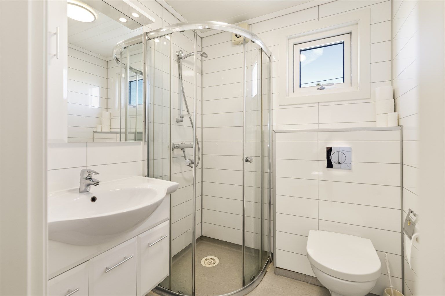 Badet er innredet med dusjnisje, vegghengt toalett og servant med underskap.