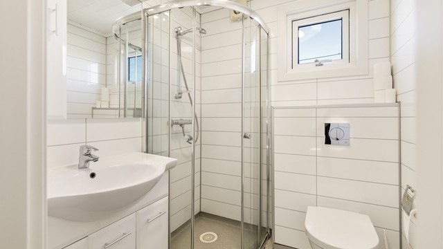 Badet er innredet med dusjnisje, vegghengt toalett og servant med underskap.