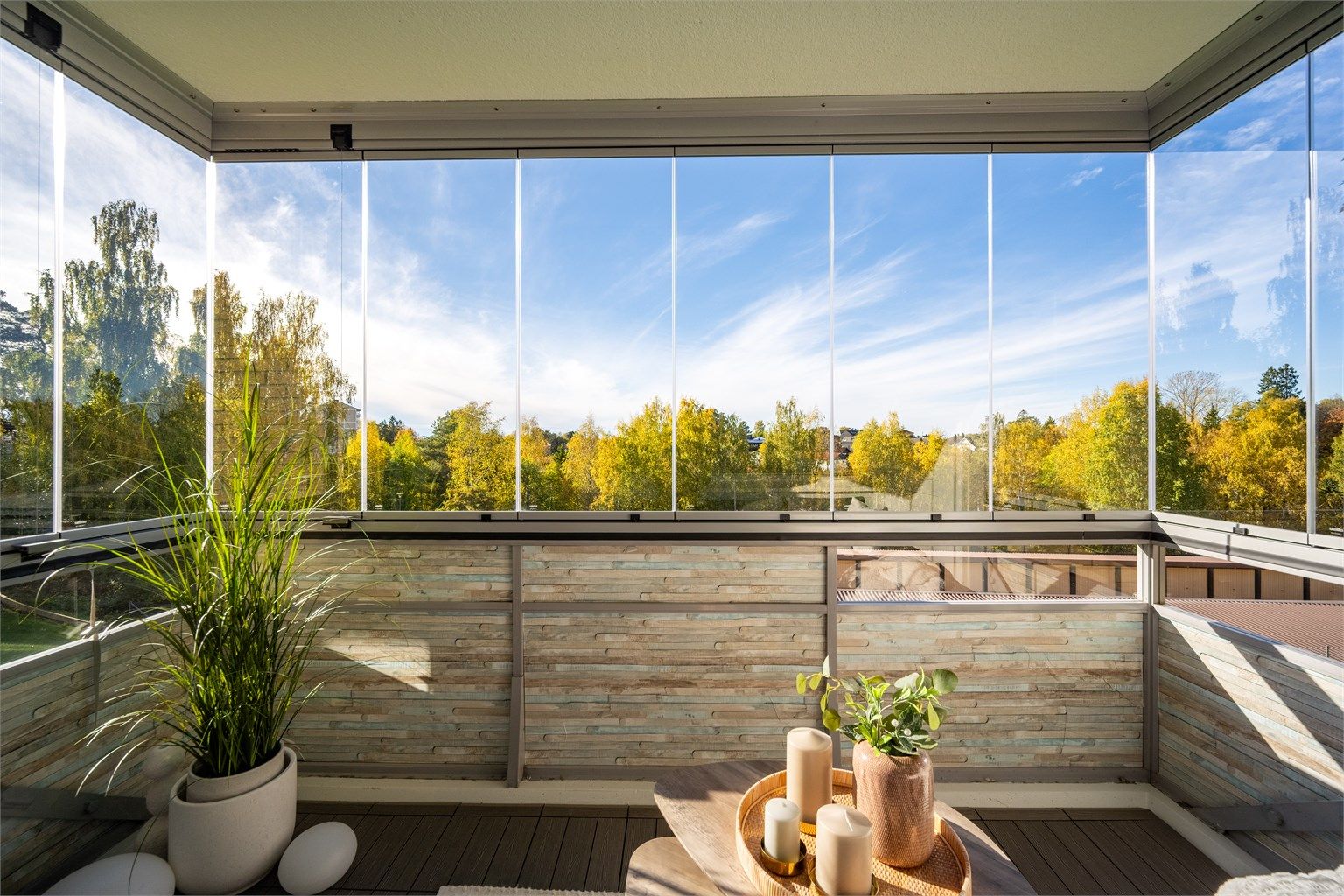Vestvendt innglasset balkong med utsikt mot grønne fellesarealer og trær.