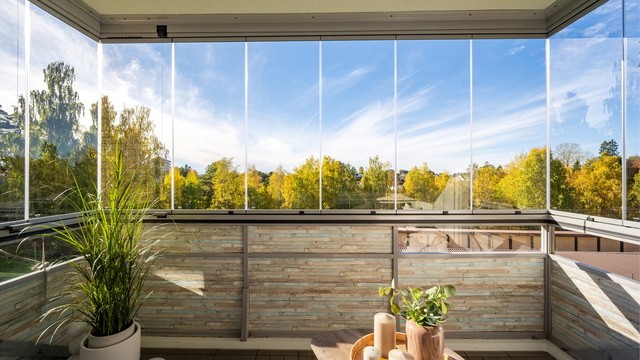 Vestvendt innglasset balkong med utsikt mot grønne fellesarealer og trær.