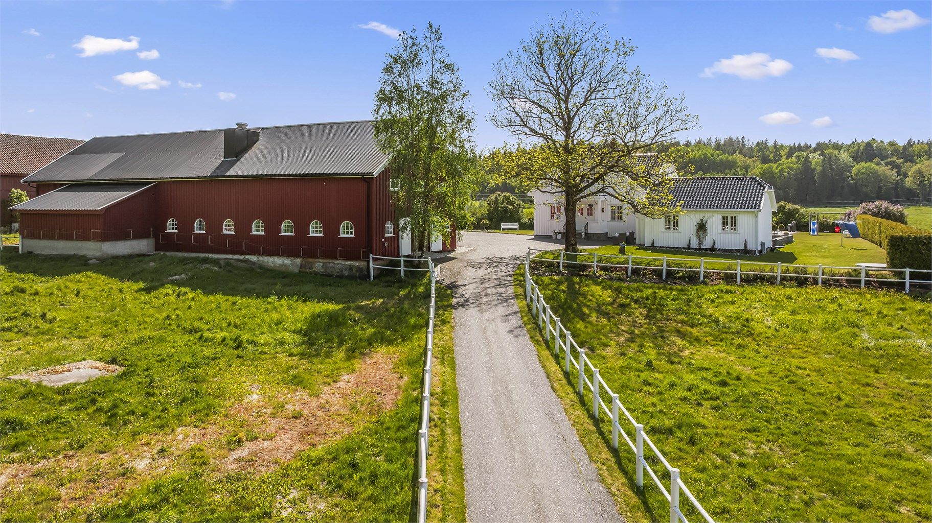 Man kjører inn fra Åsrumveien og inn på egen eiendom. Asfaltert vei inn med PVC-hestegjerder på hver side av veien.