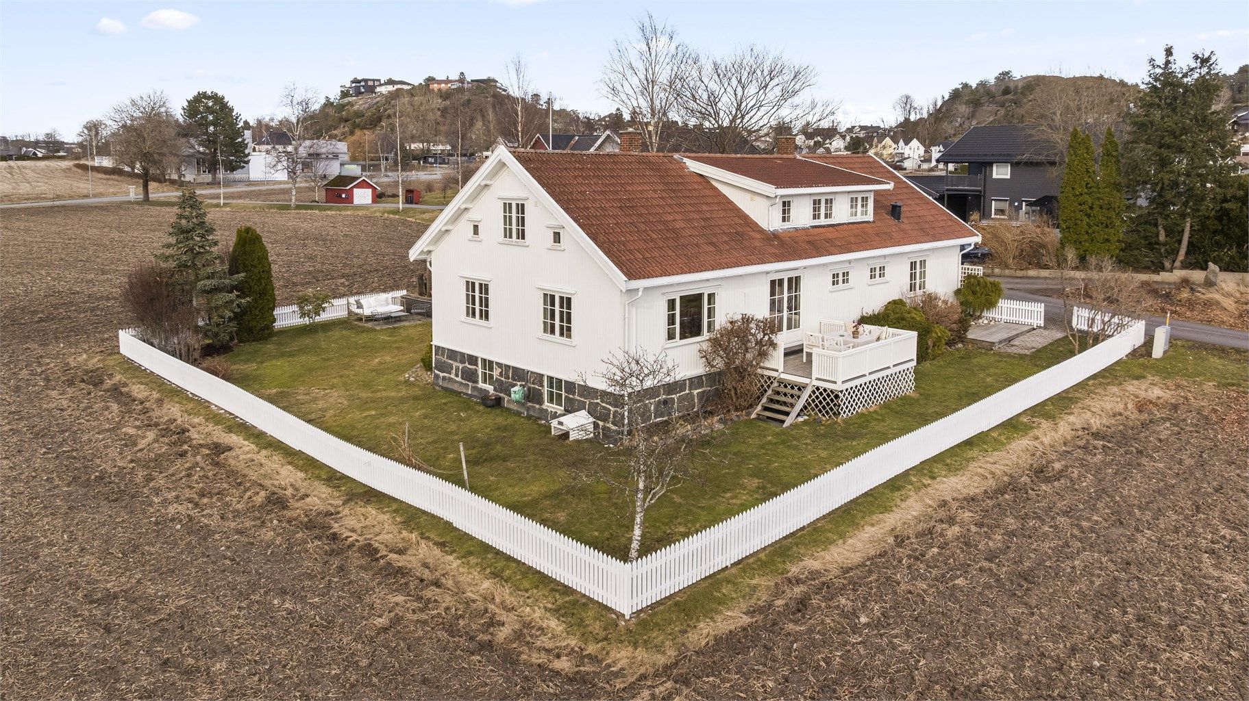 Eiendommen er omkranset av et hvitt stakittgjerde og grenser mot friarealer.