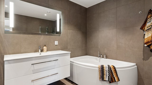 Flislagt gulv med gulvvarme, downlights i taket og servant i innredning.