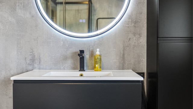Badet har baderomsplater på veggene og en moderne, mørk innredning.