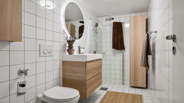 Innbydende og meget romslig bad med lyse fliser, varmekabler i gulv og opplegg for vaskemaskin