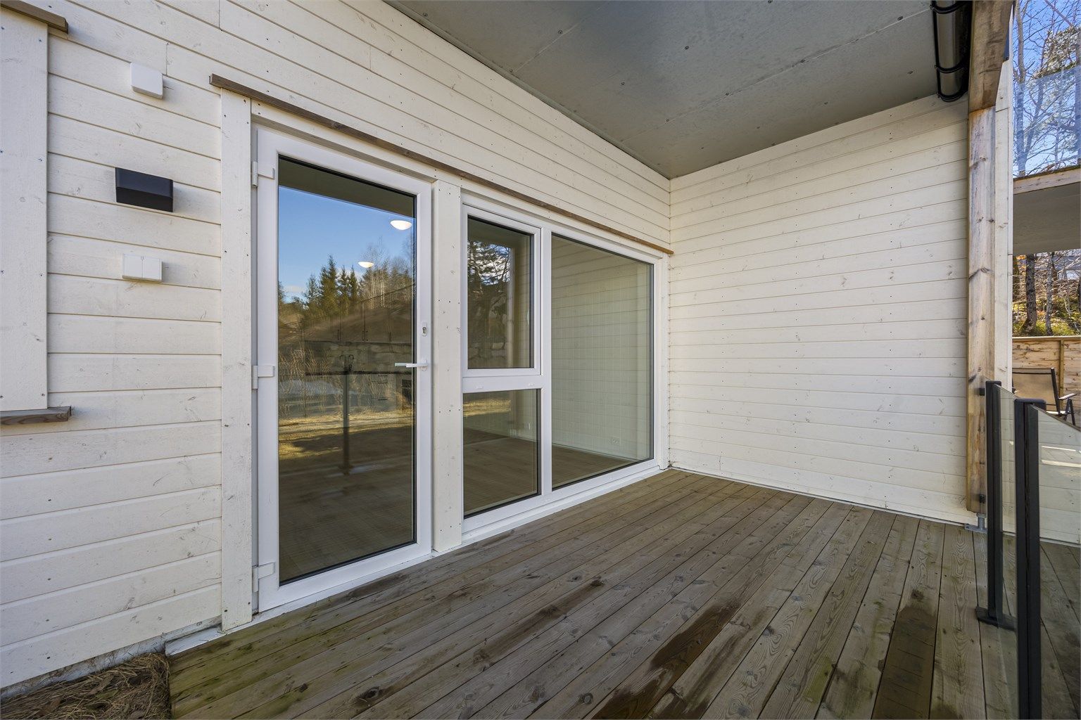 Flott terrasse med takoverbygg og glassrekkverk.