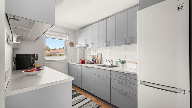 Innredningen har slette fronter og laminatbenkeplater langs to vegger, noe som gir gode arbeidsflater. Under overskapene er det benkebelysning og stikkontakter.