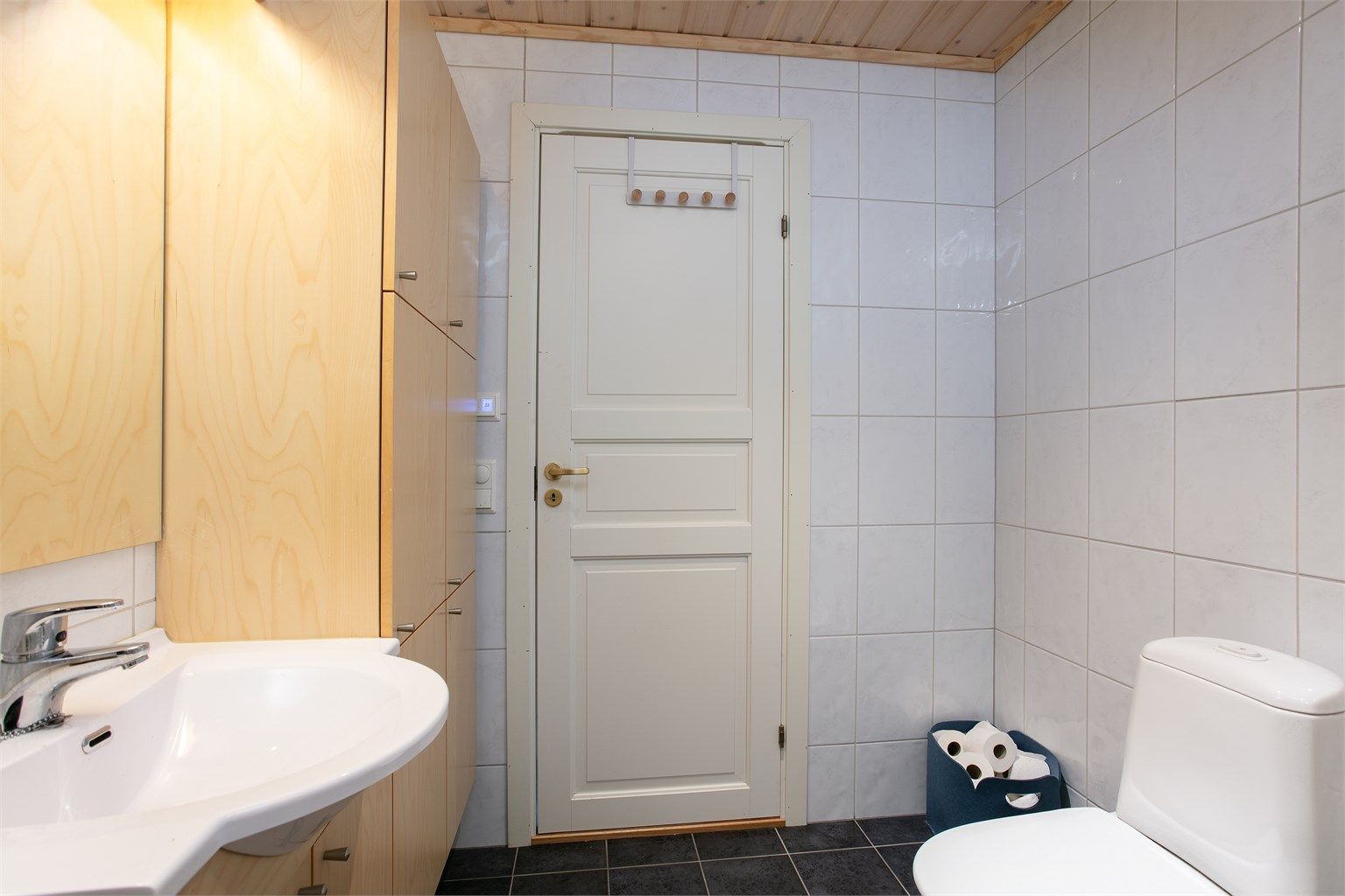 Helhetsinntrykk av badet med flislagte overflater og profilert innerdør.