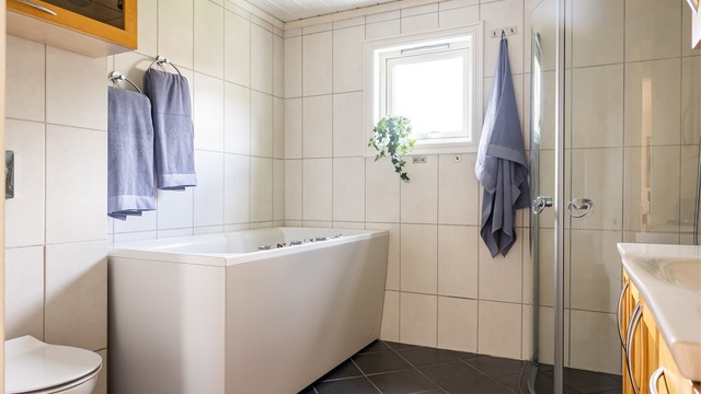 Badet er av god størrelse, med flislagte overflater, gulvvarme, vegghengt toalett, dusj og et ekslusivt Hurricane boblebad