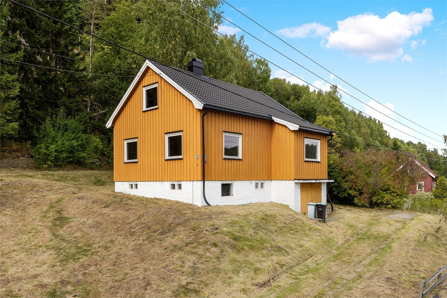 Eiet tomt i skrånende terreng opparbeidet med plen og omkringliggende vegetasjon.