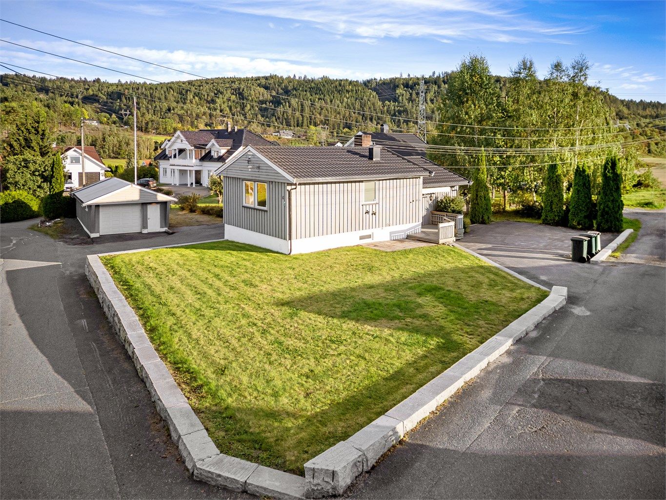 Tomten er pent opparbeidet med asfalterte innkjøringer, plen, busker, trær og noe beplantning