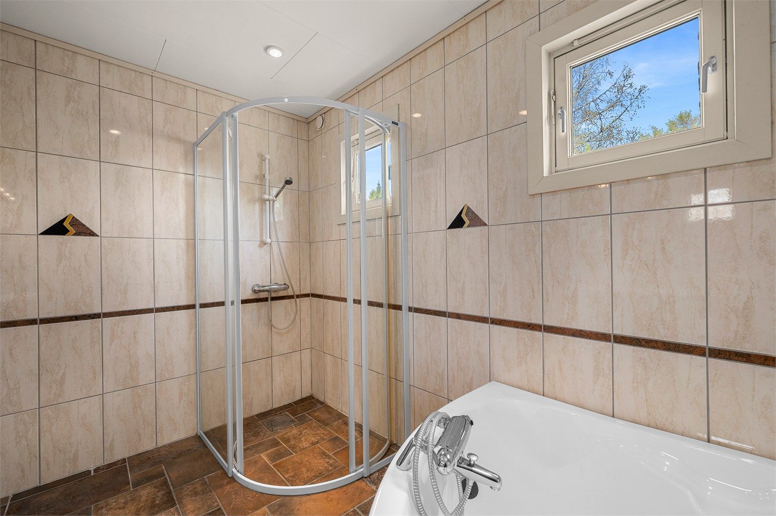 Badet måler 7 kvm og er innredet med servantskap med speil og lys, badekar og dusjhjørne. 