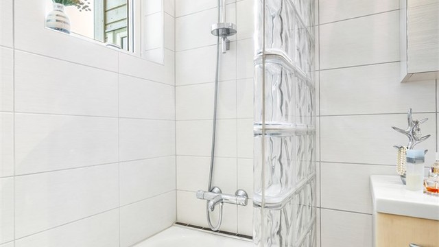 Innmurt badekar med hånddusj og skjermvegg i glassbyggerstein.