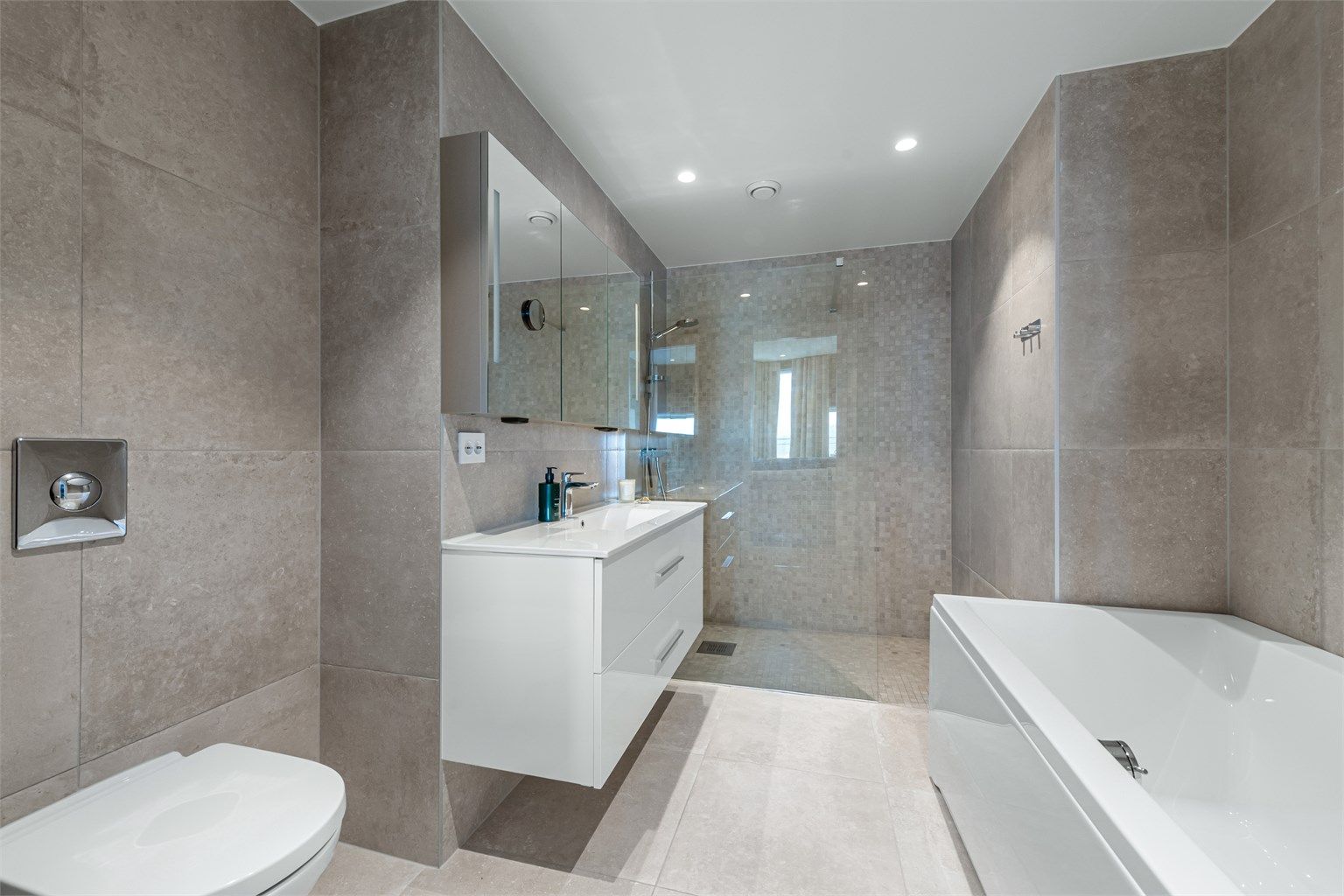 Flott bad i tilknytning til hovedsoverom. Baderomsinnreding med skuffer og ovenpåliggende servant. Speilskap over servant. Frittstående badekar og vegghengt toalett. Dusjnisje med glassvegg og vegghengt dusjarmatur