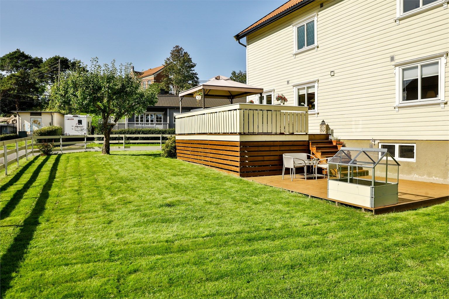 Hagen er lettstelt, solfylt dagen gjennom sommerstid og pent rammet inn av gjerde oppført i 2018. Plattingen ble anlagt i 2010. Bildet er tatt i 2019 og viser eiendommen sommerstid.