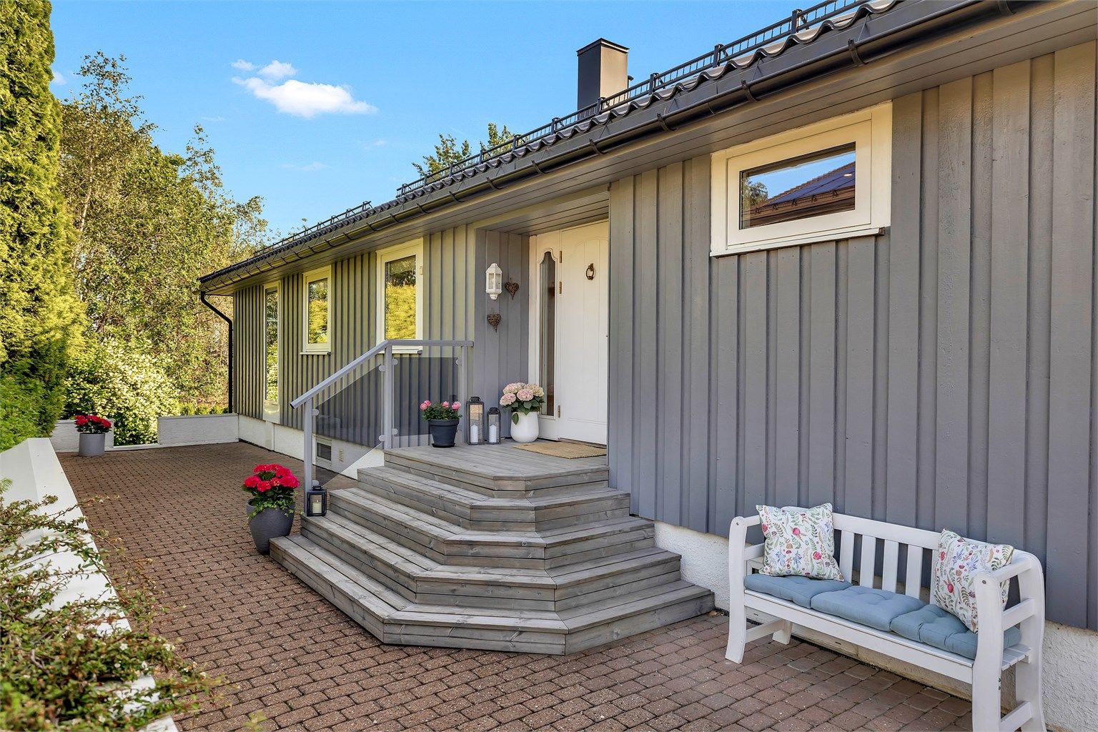 Pent og innbydende inngangsparti med trapp i treverk. Området er opparbeidet med belegningsstein, blomster og sittebenk som skaper en hyggelig og hjemmekoselig velkomst. 