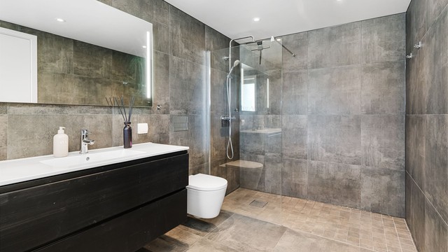 Romslig dusjsone med glassvegg og en helhetlig moderne finish