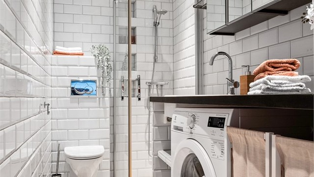Badet er innredet med benkeplate av tre med nedfelt servant av porselen, vegghengte skap med speil over servant og dusjhjørne med innfellbare glassdører.