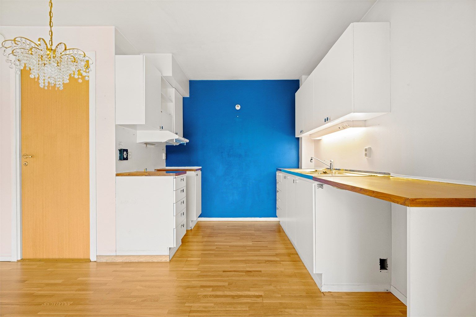 Kjøkkeninnredning med glatte fronter, ventilator i overskap og benkeplate i laminat med god belysning.