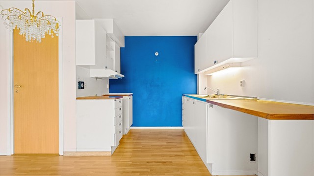 Kjøkkeninnredning med glatte fronter, ventilator i overskap og benkeplate i laminat med god belysning.