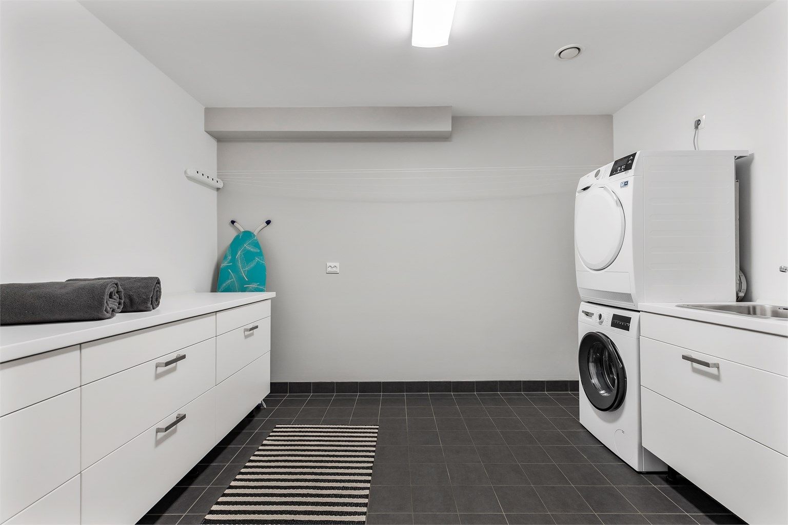 Vaskerom med flislagt gulv med varme og vegger i malte flater. Baderomsinnredning med slette fronter. Benkeplate av laminat. Nedfelt oppvaskkum av rustfritt stål med ett-greps. Mekanisk avtrekksventil på vegg. Opplegg for vaskemaskin/tørketrommel.