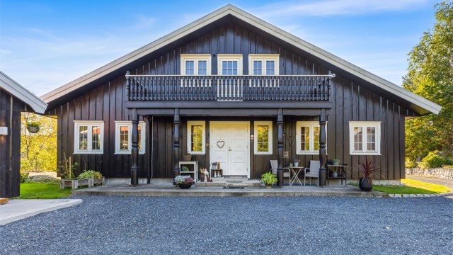 Boligens inngangsfasade med overbygd svalgang, balkong i 2. etasje og gruset gårdsplass.